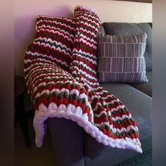 there is a blanket on the couch next to some pillows and a pillow cover that has been crocheted