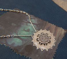 a silver necklace with an intricate design on it's chain, sitting on top of a piece of leather