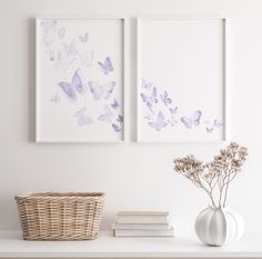 two paintings on the wall above a shelf with flowers and books in front of them