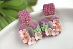 two pink earrings with flowers on them sitting on a plate