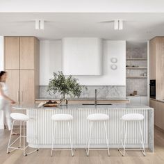 a woman standing in front of a kitchen island with three stools next to it