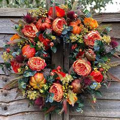 a wreath with orange flowers and greenery hangs on a wooden fence