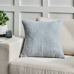 a blue pillow sitting on top of a couch next to a vase with a plant