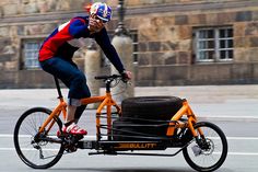 a man riding on the back of an orange bike with a cart attached to it