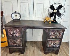 an old desk with graffiti on it and a fan sitting next to it, in front of a white door