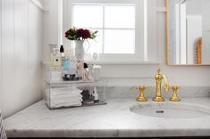 a bathroom sink with gold faucet and marble counter top next to a window