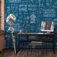 a desk with a computer on it in front of a blueprinted wallpaper