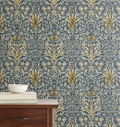 a blue and gold wallpaper with an ornate design on the sideboard next to a wooden dresser