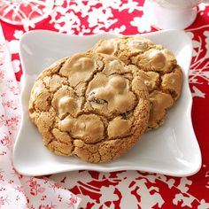 two chocolate chip cookies on a white plate with red and white table cloth behind them