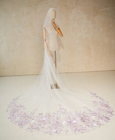 a mannequin wearing a wedding dress and veil with purple flowers on the floor