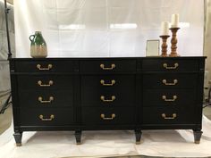 a black dresser with gold handles and knobs on it's sides, in front of a white backdrop