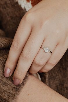 a woman's hand with a diamond ring on her left wrist, wearing a brown sweater