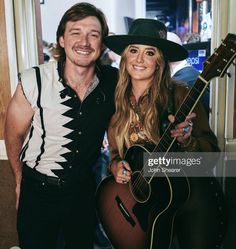 a man and woman posing for a photo while holding guitars in front of the camera