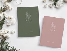 two books sitting next to each other on top of a table with white flowers and greenery