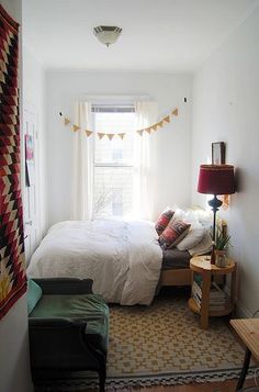 a small bedroom with a bed, desk and lamp in it's corner next to a window