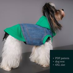 a small white dog wearing a green shirt and blue jean jacket on it's back