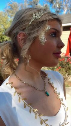 a woman in white shirt wearing gold jewelry and head piece with leaves on her face