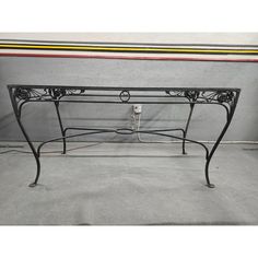 a wrought iron table with a colorful stripe on the top and bottom part, in front of a gray wall