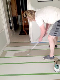 a man in white shirt and gray shorts painting a room with green stripes on the floor