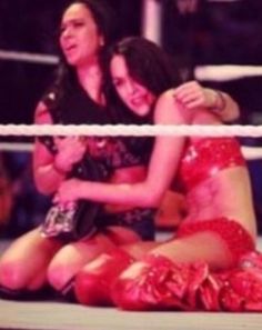 two women sitting on the ground with their arms around each other in a wrestling ring