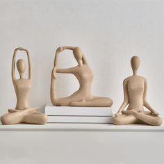 three clay figures sitting on top of books in the shape of people doing yoga poses