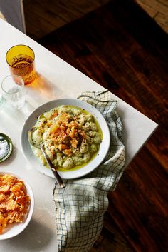 a table topped with plates of food next to two glasses filled with liquid and seasonings