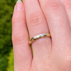 a woman's hand with a gold wedding ring on her left and green grass in the background