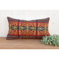 a red and yellow pillow sitting on top of a wooden table next to a plant