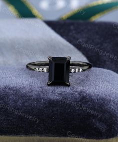 an emerald cut black diamond ring sitting on top of a blue and white velvet cushion