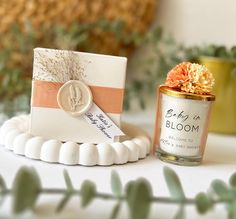 a small candle and some flowers on a white table with green plants in the background