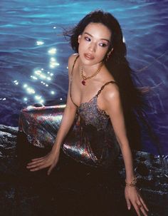 a woman sitting in the water with her hair blowing back and looking at the camera