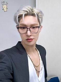 a person wearing glasses and a black blazer sitting in front of a computer desk