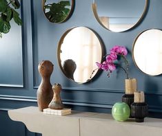 three mirrors on the wall above a table with vases and flowers