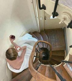 a woman sitting on top of a wooden staircase next to a spiral stair case in a building