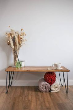 a wooden table topped with two blankets and a vase filled with dried flowers on top of it