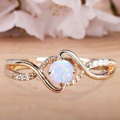 a white opalite and diamond ring sitting on top of a table next to flowers