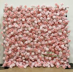 a wall made out of pink flowers on top of a wooden floor in front of a white wall