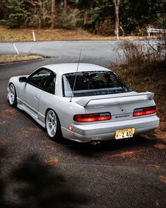 a white car parked on the side of a road in front of some trees and bushes