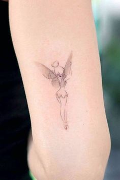 a woman's arm with a small fairy tattoo on the back of her shoulder