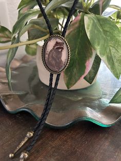 This awesome bolo tie has a vintage raccoon print with a clear resin coating and metal backing. Handmade in our shop!The cord is black and made of genuine woven leather.Our bolos pair nicely with many of our belt buckles! They make wonderful gifts.The western bolo tie rope length is 39'' ; pendant size is 1 1/2'' x 1 1/4'' Vintage Style Adjustable Bolo Ties As Gifts, Vintage Black Jewelry For Western-themed Events, Vintage Black Bolo Ties For Gift, Vintage Black Bolo Ties As Gift, Black Adjustable Bolo Tie, Adjustable Black Bolo Tie, Black Bolo Tie With Adjustable Cord, Black Bolo Tie With Adjustable Cord As Gift, Handmade Adjustable Unique Bolo Ties