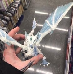 a hand holding a small white and blue dragon figurine in a book store