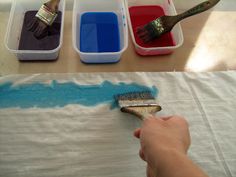 someone is painting with blue and red paint on the table next to two plastic containers