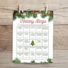 a holiday bingo game is hanging on a wooden wall with pine branches and evergreens