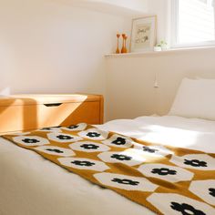 a bed with white sheets and black flowers on it, next to a wooden dresser