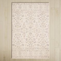 a white rug with an intricate design on the top and bottom, in front of a wooden wall