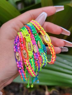 a hand holding several colorful bracelets on it's palm tree branch with white nail polish