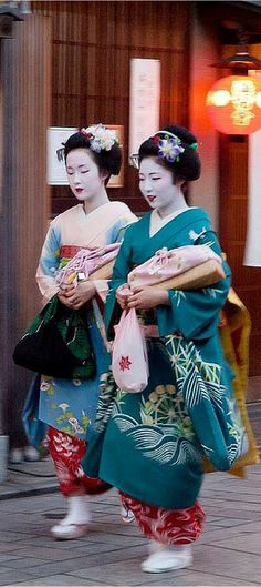 two geisha walking down the street carrying bags