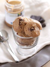 two chocolate chip ice creams in a glass bowl next to a jar of peanut butter