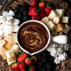 a chocolate dip surrounded by marshmallows, strawberries, and other foods