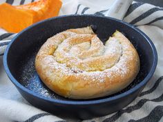 a pastry in a skillet with powdered sugar on the top and an orange slice next to it